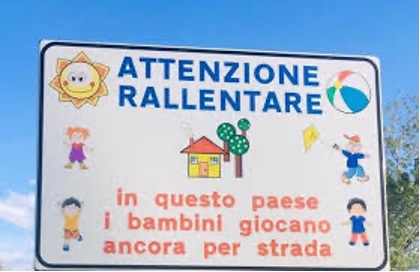 Image of traffic sign in Italian with images of sunshine with smiling face, a ball a house and a tree and 4 children playing. The message on the sign to motorists is translated in the English text.   
